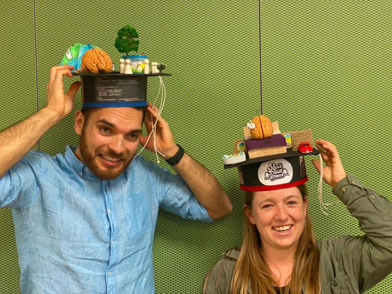 Emmanuel and Mirjam wear their doctoral hats, which represent the contents of their dissertations, e.g. a bed and brain on Mirjam's hat and a brain and globe on Emmanuel's hat.