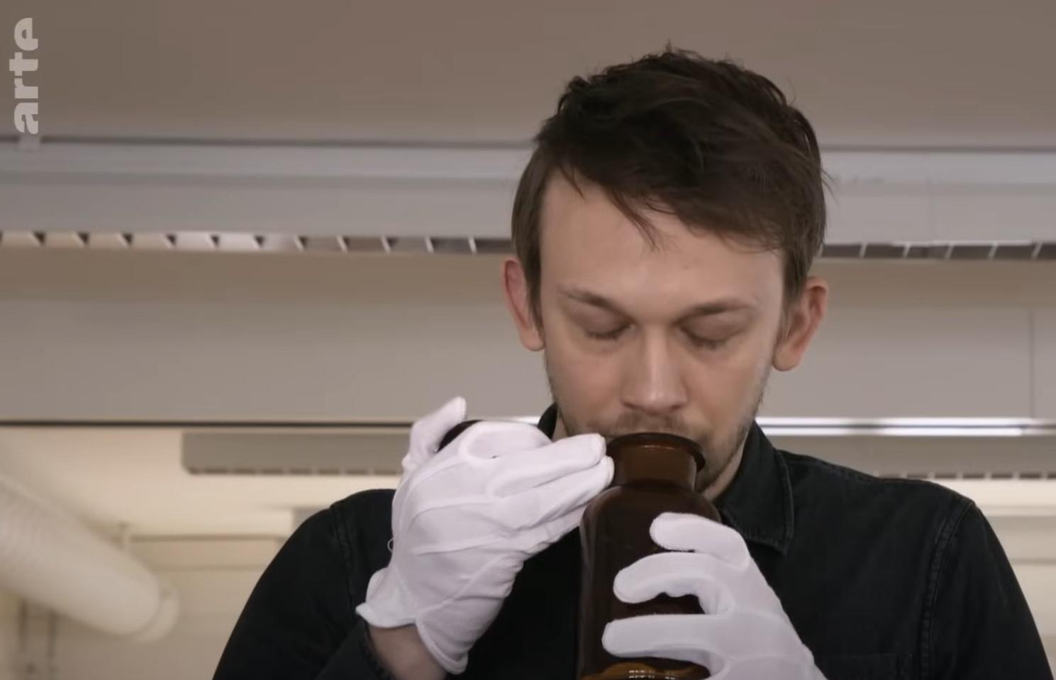 Ein Mann riecht an einer Flasche, welche den Geruch einer Frau auf einem Wattebausch enthält.
